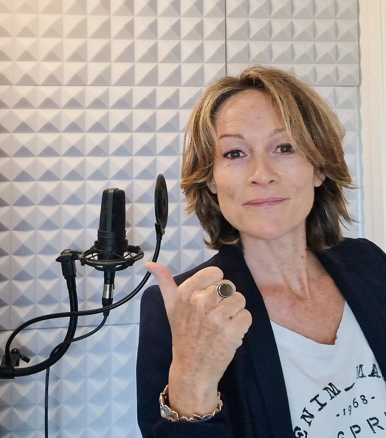 Een studio-microfoon naast een laptop waarop digitale geluidsgolven te zien zijn.